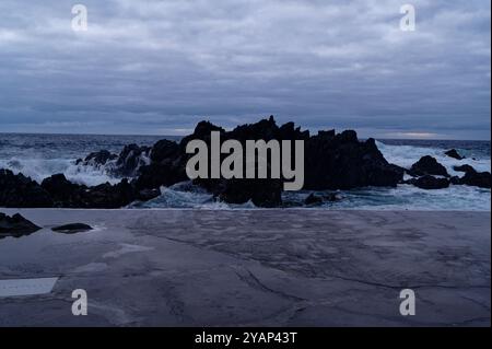 Die Wellen brechen unter einem dramatischen Himmel an den natürlichen Pools von Porto Moniz gegen vulkanische Felsen Stockfoto