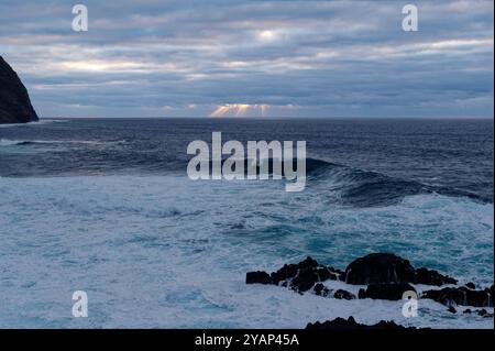 Sonnenstrahlen brechen durch die Wolken über dem atlantik und werfen ein ruhiges Licht auf die Wellen vor Madeiras dramatischer Küste Stockfoto