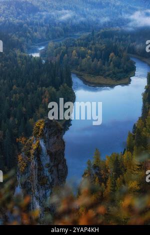 Ein ruhiger Fluss fließt sanft durch einen grünen Wald bei Sonnenaufgang, der von beeindruckenden felsigen Klippen und lebhaftem Herbstlaub hervorgehoben wird Stockfoto