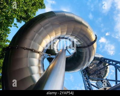 Geschwungene Metallschienenkonstruktion, die zum blauen Himmel und Baum führt Stockfoto