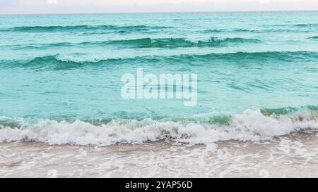 Atemberaubende Aussicht auf azurblaue Meereswellen, die sanft auf einen unberührten Sandstrand stürzen und ein Gefühl der Entspannung und Flucht wecken. Das Bild vermittelt die Idee o Stockfoto