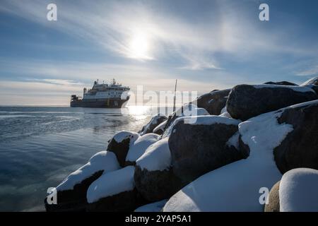 Anticosti Island, Québec, Kanada – 7. Januar 2024: Ein großes Frachtschiff mit mehreren Etagen, Kran und Containern segelt im Ozean und kommt an einem Po an Stockfoto