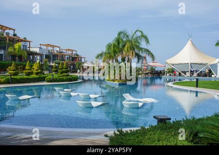 Ein ruhiges Resort verfügt über einen atemberaubenden Pool, der von üppigen Pflanzen und modernen Liegestühlen flankiert wird und an einem perfekten Tag unter hellem Himmel zum Entspannen einlädt. Stockfoto