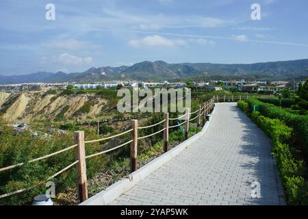 Ein friedlicher, von Holzschienen gesäumter Weg lädt Wanderer ein und bietet einen atemberaubenden Blick auf die sanften Hügel und den hellblauen Himmel mit weichen Wolken. Stockfoto