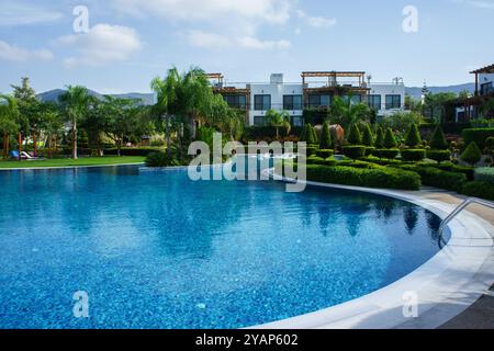 Eine ruhige Umgebung entfaltet sich mit einem glitzernden blauen Pool, der den klaren Himmel reflektiert, umgeben von gepflegten Gärten und luxuriösen Villen mit elegantem Ar Stockfoto