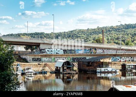 Belgrad, Serbien - 15. September 2019: Schwimmende Häuser unter einer Graffiti-überdachten Brücke in Ada Ciganlija Stockfoto