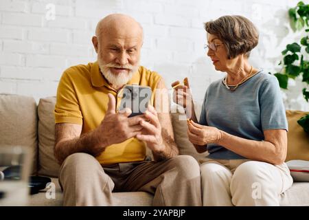 Eine hingebungsvolle Ehefrau hilft ihrem Mann mit Diabetes, während sie mit seinem Smartphone interagiert. Stockfoto