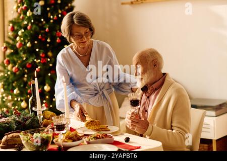 Ein Seniorenpaar genießt ein gemütliches Weihnachtsessen, umgeben von Dekorationen und festlichem Essen. Stockfoto