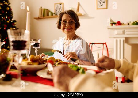 Eine ältere Frau lächelt hell, während sie mit ihrem Partner ein köstliches Weihnachtsessen genießt. Stockfoto