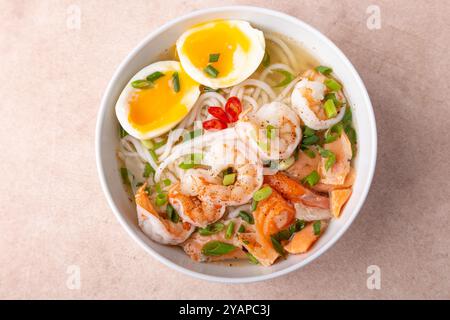 Asiatisches Gericht mit Brühe, Nudeln, Tigergarnelen, Fisch, Ei und grünen Zwiebeln. Traditionelle asiatische Suppe auf einem weißen, tiefen Teller. Selektiver Fokus, Nahaufnahme. Stockfoto