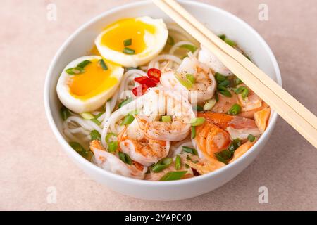 Asiatisches Gericht mit Brühe, Nudeln, Tigergarnelen, Fisch, Ei und grünen Zwiebeln. Traditionelle asiatische Suppe auf einem weißen, tiefen Teller. Selektiver Fokus, Nahaufnahme. Stockfoto