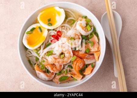 Asiatisches Gericht mit Brühe, Nudeln, Tigergarnelen, Fisch, Ei und grünen Zwiebeln. Traditionelle asiatische Suppe auf einem weißen, tiefen Teller. Selektiver Fokus, Nahaufnahme. Stockfoto