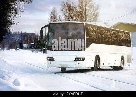 Weißer Reisebus, der an einem Winternachmittag in der Zeit der goldenen Stunde auf einer verschneiten Straße in der Stadt fährt. Stockfoto