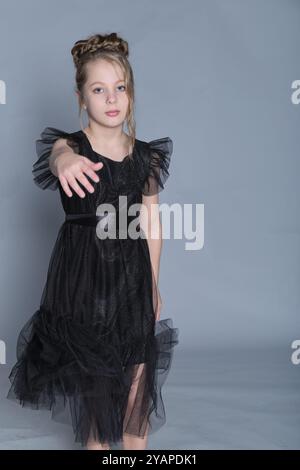 Ein junges Mädchen tanzt anmutig in einem schwarzen Tüllkleid und streckt ihren Arm mit Elan und Eleganz nach vorne. Dieses Bild fängt die Schönheit der Bewegung ein Stockfoto