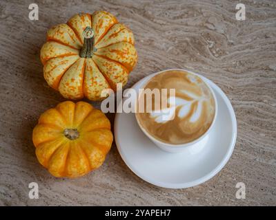 Kürbis-Gewürz-Latte. Weiße Kaffeetasse mit cremigem Schaum, kleine orangene Kürbisse am Marmortisch. Stockfoto