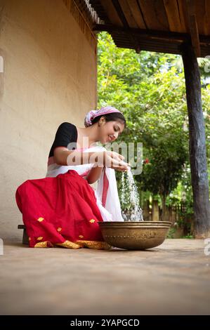 Ein assamesisches Mädchen trennt eifrig Schale von Reis mit einer traditionellen Dola und Saloni, wodurch das zeitlose Erbe ihres Dorfes bewahrt wird. Stockfoto