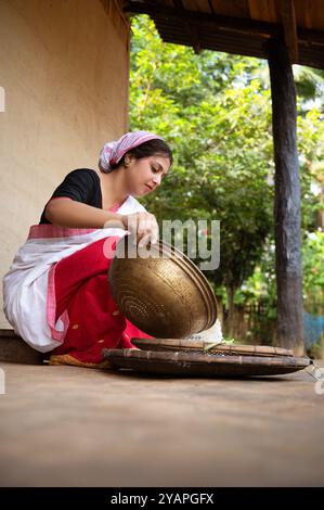 Ein assamesisches Mädchen trennt eifrig Schale von Reis mit einer traditionellen Dola und Saloni, wodurch das zeitlose Erbe ihres Dorfes bewahrt wird. Stockfoto