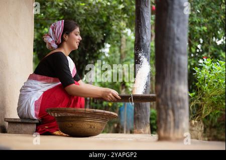 Ein assamesisches Mädchen trennt eifrig Schale von Reis mit einer traditionellen Dola und Saloni, wodurch das zeitlose Erbe ihres Dorfes bewahrt wird. Stockfoto