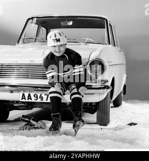 Eishockey in den 1960ern Ein Junge sitzt auf der Vorderseite eines Opel Kadett Autos und zieht seine Schlittschuhe in seiner Eishockeyausrüstung an. Er ist bereit, Eishockey zu spielen. 1963. Kristoffersson Ref. DE1-2 Stockfoto