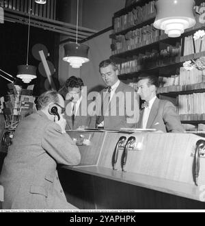 Wie Sie Platten in den 1950ern gekauft haben Der Mann, der ein Telefon hält, hört sich tatsächlich eine Aufzeichnung an. Zu dieser Zeit war es üblich, dass die Kunden die Aufzeichnungen im Store anhören konnten, bevor sie sich für den Kauf entschieden. Der Plattenladen verfügt über mehrere Abhörstationen und die Mitarbeiter hinter dem Schalter, die das System verwalten. Dieses Geschäft ist die Selanders Skivbar auf der Vasagatan in Stockholm. 1955. Stockfoto