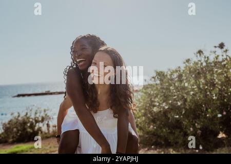 Zwei junge Frauen lächeln und lachen, während eine von ihnen die andere auf ihrem Rücken trägt Stockfoto