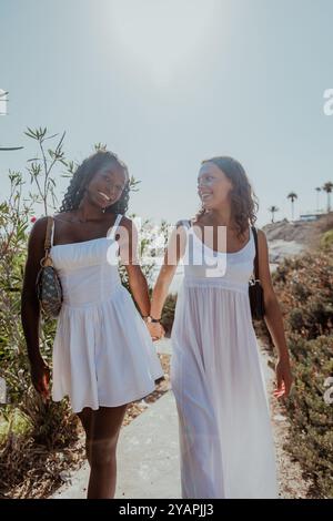 Zwei Frauen gehen zusammen auf einem Weg, halten Hände lächelnd, vertikales Foto. Stockfoto