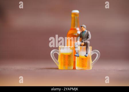 Kreativszene mit einem kleinen Geschäftsmann, der mit einer Flasche dahinter auf Bierbechern sitzt und Themen wie Freizeit und Balance beleuchtet. Stockfoto