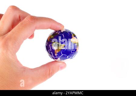 Nahaufnahme einer Hand, die einen Globus in Form eines Puzzleteils hält, der globale Einheit und Vielfalt auf einem hellen weißen Hintergrund symbolisiert. Stockfoto