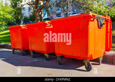 Drei leuchtend orangefarbene Mülltonnen auf einer Straße in Kiew mit Grün im Hintergrund. Stockfoto