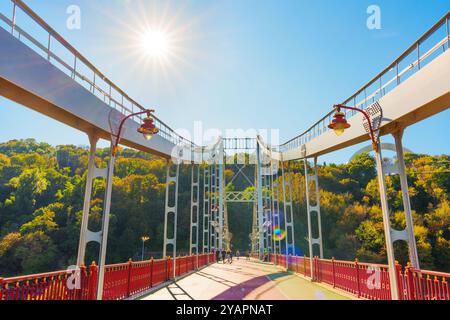 Kiew, Ukraine - 9. Oktober 2024: Helles Sonnenlicht beleuchtet die Parkovyy-Brücke in Kiew, umgeben von üppigem Grün. Ein perfekter Herbsttag zum Spazierengehen Stockfoto