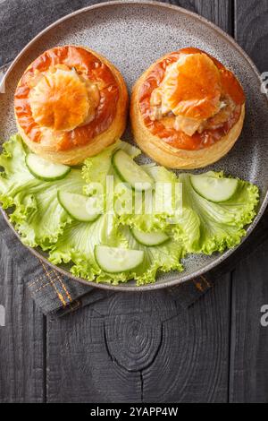 Französischer Bouchee-Blätterteig mit Kalbfleisch in scharfer Sauce serviert mit Salat und Gurke in Nahaufnahme auf einem Teller auf einem Holztisch. Vertikale Draufsicht Stockfoto