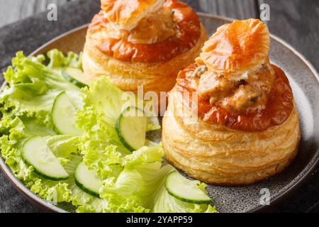 Mit Rindfleisch gefüllte french vol au Vent serviert mit Salat und Gurke in Nahaufnahme auf einem Teller auf einem Holztisch. Horizontal Stockfoto