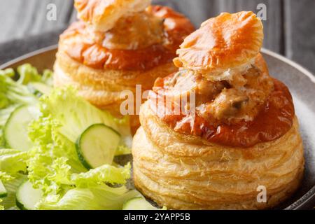 Blätterteig Bouchee oder vol-au-Vent mit Kalbsfleisch in scharfer Sauce serviert mit Salat und Gurke in Nahaufnahme auf einem Teller auf einem Holztisch. Horizontal Stockfoto