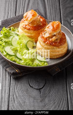 Bouchee a la reine oder vol-au-Vent mit Kalbfleisch in scharfer Sauce serviert mit Salat und Gurke in Nahaufnahme auf einem Teller auf einem Holztisch. Vertikal Stockfoto