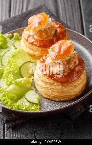 Französischer Bouchee-Blätterteig mit Kalbfleisch in scharfer Sauce serviert mit Salat und Gurke in Nahaufnahme auf einem Teller auf einem Holztisch. Vertikal Stockfoto