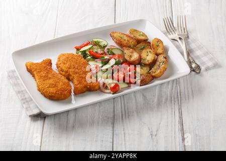 Knuspriger panierter Weißfisch mit frischem Salat und gebratenen Kartoffeln im Landhausstil in Nahaufnahme auf einem Teller auf einem Holztisch. Horizontal Stockfoto
