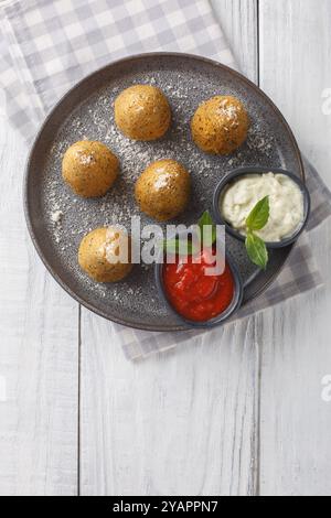 Sizilianische Reisbällchen konisch geformte Arancini, gefüllt, mit Brotkrumen beschichtet und frittiert, serviert mit zwei Soßen in Nahaufnahme auf einem Teller auf einem hölzernen Ta Stockfoto