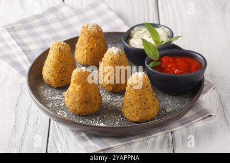 Reisbällchen, auch Arancini genannt, serviert mit zwei Soßen in Nahaufnahme auf einem Teller auf einem Holztisch. Horizontal Stockfoto