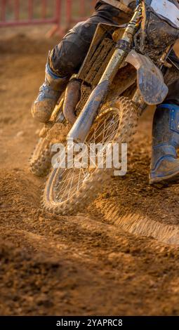 Detail der Vorderseite eines Off-Road-Motocross-Bikes, das in schlammigem Gelände eine Kurve umfährt, wobei die Räder und die Stiefel des Fahrers von Schlamm verschmutzt sind. Stockfoto