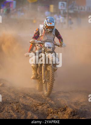 Motocross-Fahrer in Aktion, der in einem Dauerrennen eine unbefestigte Straße hinunterfährt und mit seinem Hinterrad viel Staub erzeugt. Stockfoto