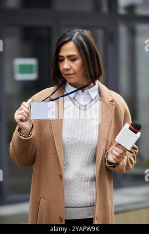 Eine multirassische Journalistin steht draußen, hält ein Mikrofon und zeigt ihr Presseabzeichen, bereit, zu berichten. Stockfoto