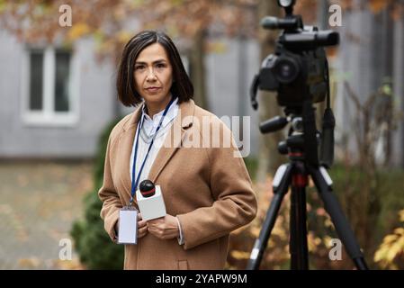 Eine multirassische Journalistin steht zuversichtlich mit einem Mikrofon, bereit, im Herbst zu berichten. Stockfoto