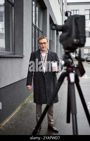 Der Journalist in Brille steht draußen und wendet sich selbstbewusst an das Mikrofon Stockfoto