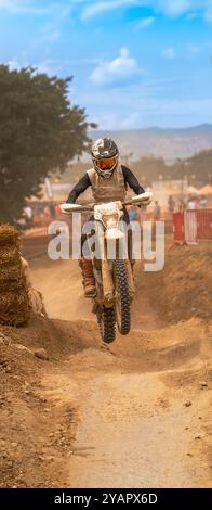 Frau, die ein Motocross-Bike mit Schlamm und Staub fährt, springt mit ihrem Motorrad über die Änderung der Steigung auf einer Feldpiste im Freien in der Halterung Stockfoto