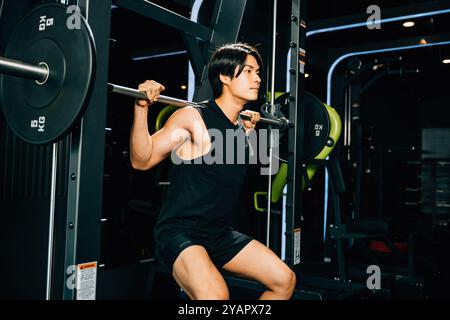 Asiatischer muskulöser Mann, der eine Hocke ausübt Beine schwere Gewichte mit einer Langhantel im Fitnessstudio, Männer Stockfoto