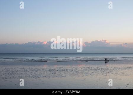 Zwei Silhouetten und kleine Hunde spazieren am Strand von Hastings bei Ebbe und Sonnenuntergang entlang. Stockfoto