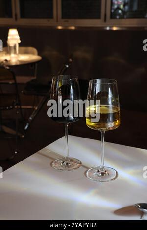 Zwei Weingläser, eins rot und eins weiß, sitzen auf einem Tisch. Der Rotwein ist fast verschwunden, während der Weißwein fast voll ist. Die Brille wird als nächstes platziert Stockfoto
