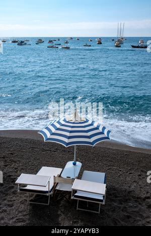 Ein ruhiger Strand erwartet Sie mit einem blau gestreiften Sonnenschirm und Liegestühlen. Stockfoto