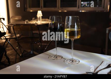 Zwei Weingläser, eins rot und eins weiß, sitzen auf einem Tisch. Der Rotwein ist fast verschwunden, während der Weißwein fast voll ist. Die Brille wird als nächstes platziert Stockfoto