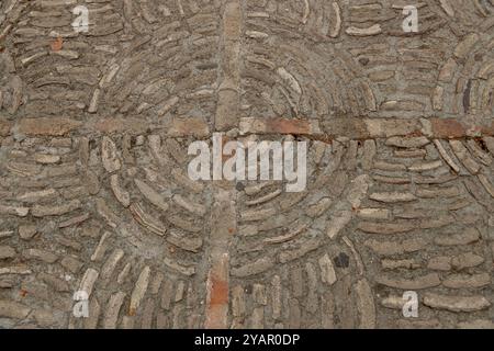 Nahaufnahme eines Steinpflasters mit kreisförmigem Ziegelmuster, das in Zement eingebettet ist. Stockfoto